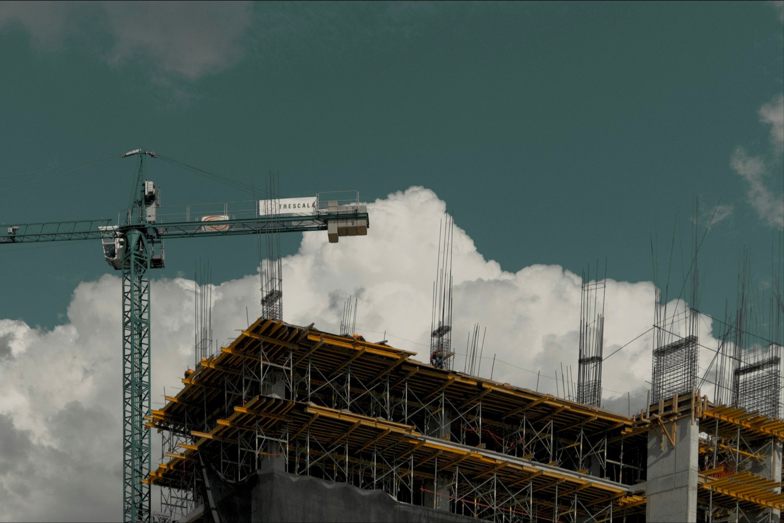 Prédio em construção com andaimes e guindaste sob céu com nuvens