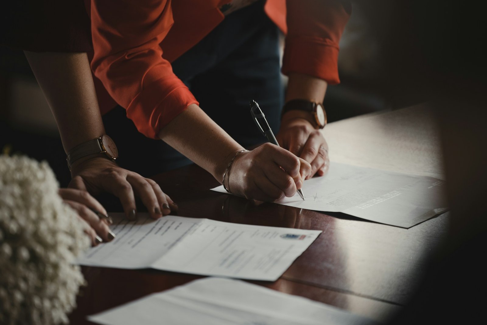 Duas pessoas assinando documentos sobre uma mesa de madeira